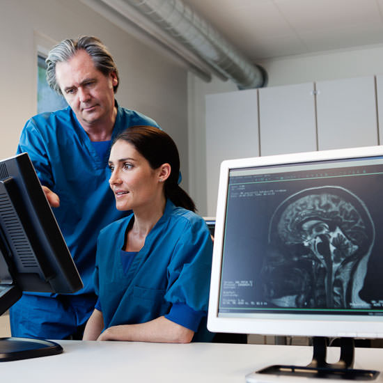 Doctor and nurse looking at computer screen with MR scan images. MR-Image of human head in foreground